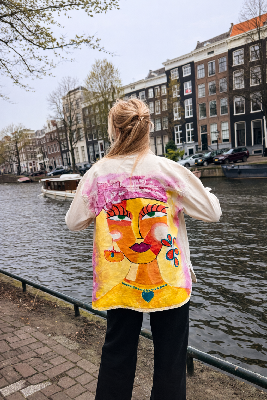 Person wearing a colorful jacket with a face design in an urban setting by a canal.