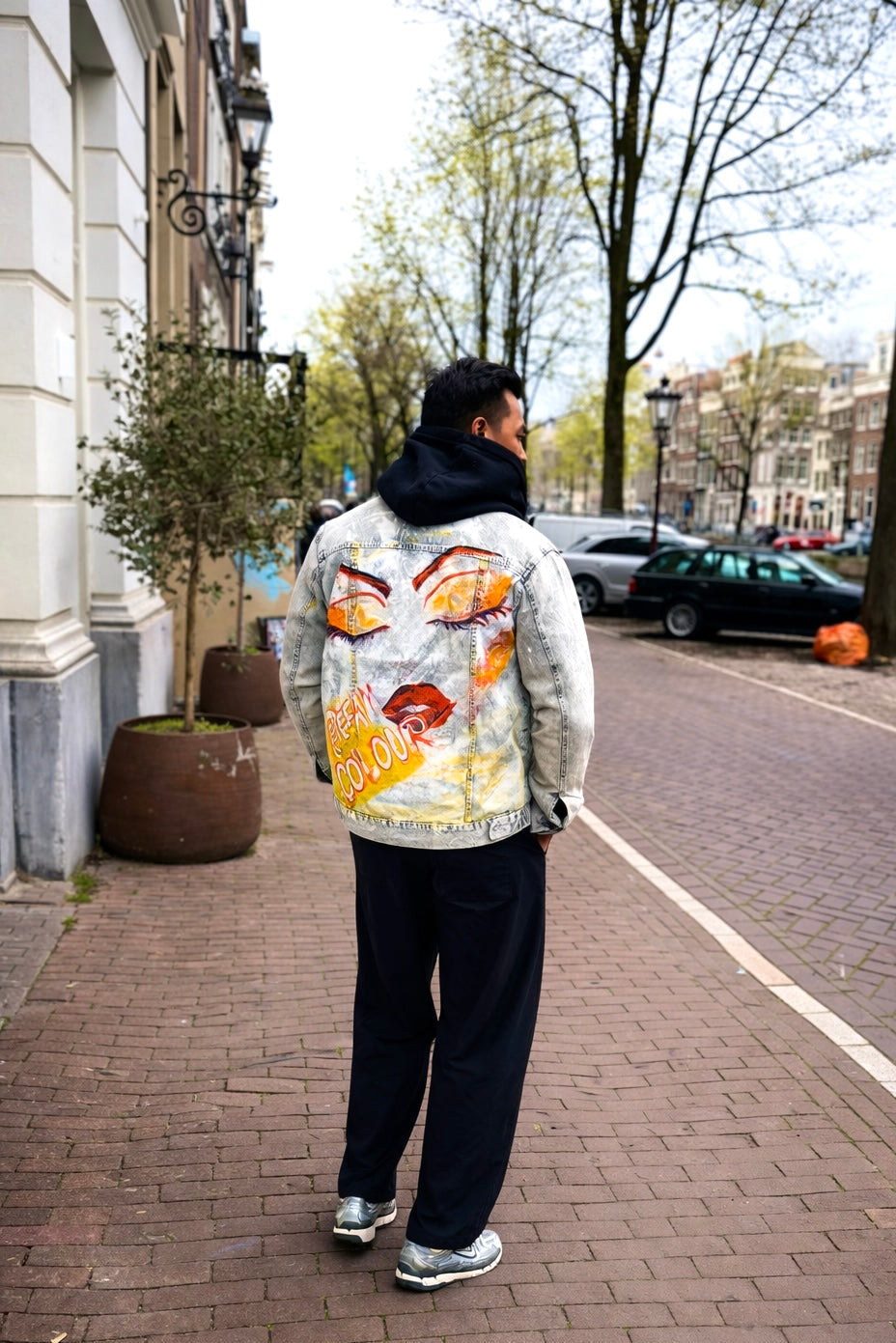 Person wearing a colorful jacket with a fish design on a city street.